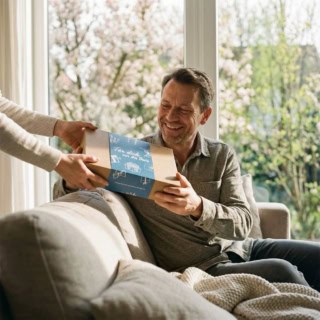 Ein Mann bekommt eine Geschenkbox der Erlebnisfabrik überreicht. - Erlebnisgeschenke für Männer.