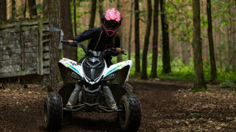 Mädchen mit rosa Helm lenkt ein Quad durch eine Offroad Strecke im Wald