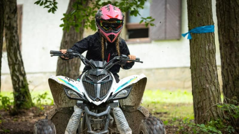 Mädchen sitzt auf Kinderquad und fährt auf Offroad Strecke zwischen Bäumen