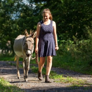 Eine Frau spaziert mit einem Esel einen Feldweg entlang.