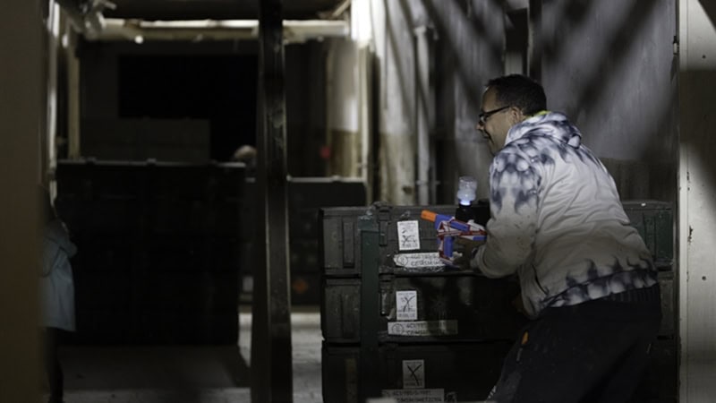 Ein Spieler mit GelBlastern in der Hand versteckt sich hinter einer Deckung