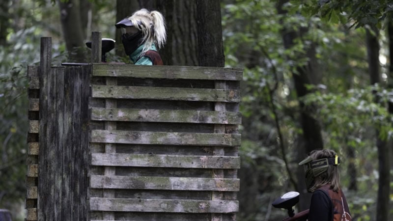 Zwei personen mit Masken und Paintballgewehren verstecken sich hinter einer großen Deckung