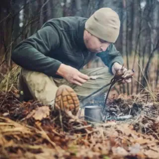 Ein Mann bereitet bei einem Survival Training Essen am Lagerfeuer zu.