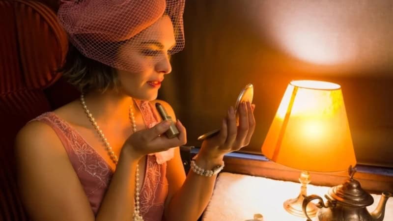 Frau im Stil der 1920er Jahre schminkt sich bei Lampenlicht.