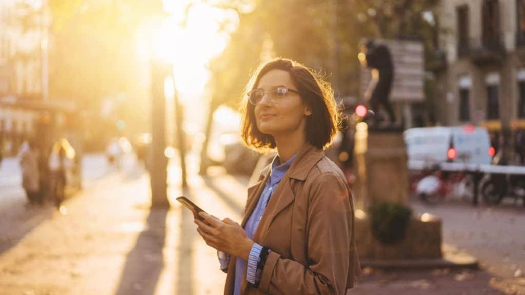 Frau mit Smartphone bei Sonnenauf- Junge Frau mit Smartphone in der Hand erkundet bei einem Sonnenuntergang die Stadt - digitale Stadtrallye.