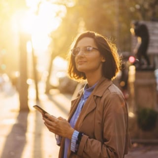 Junge Frau mit Smartphone in der Hand erkundet bei einem Sonnenuntergang die Stadt - digitale Stadtrallye.