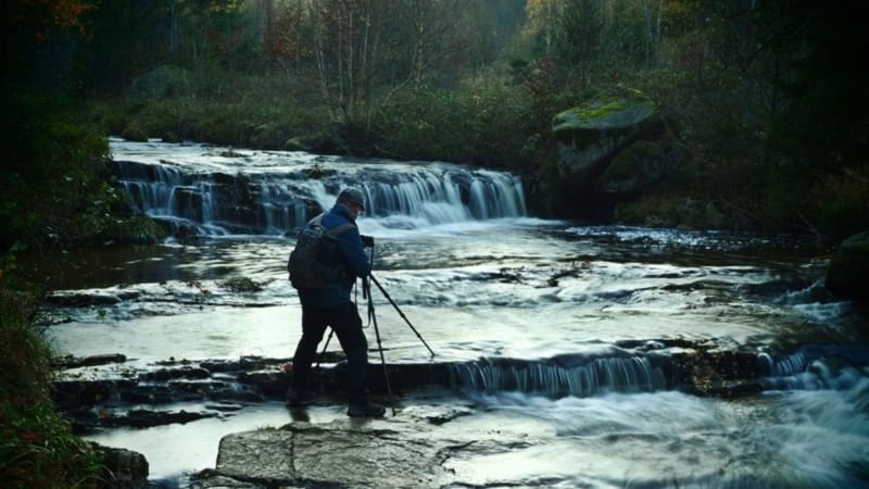 Fotograf steht im Wasser vor Wasserfall beim Fotokurs.