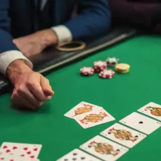 Drei Personen spielen Poker an einem grünen Tisch. Die Karten sind aufgedeckt, sodass der Gewinner ermittelt werden kann.