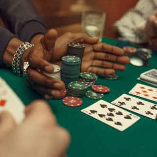 3 Personen spielen Poker mit Chips und Karten auf einem grünen Tisch.